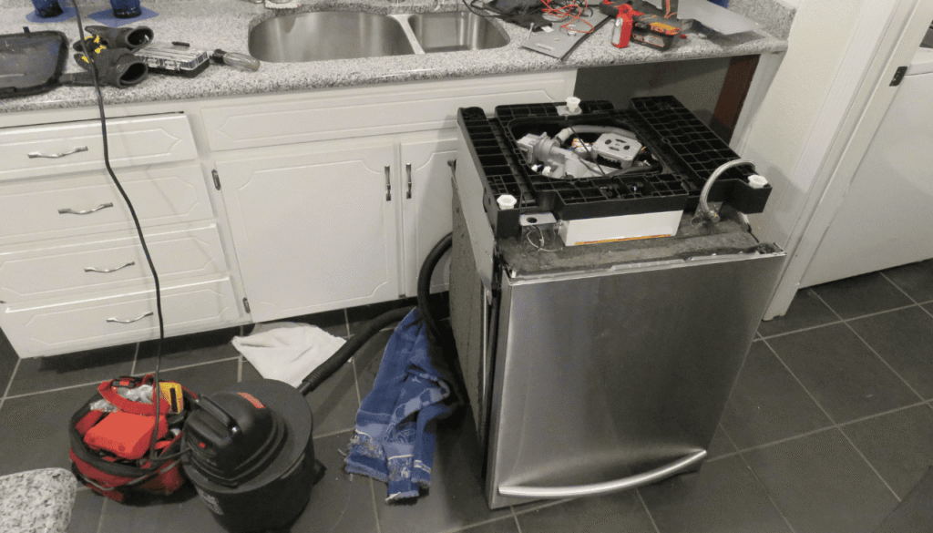 Close-up of water leaking from underneath a dishwasher, likely caused by a faulty tub seal or loose hose connection.